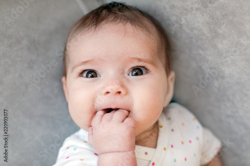 Obraz na plátně From above shot of adorable baby chewing hand and looking at camera while lying