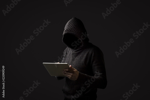 Faceless man in a hoodie with a hood holds a tablet in his hands