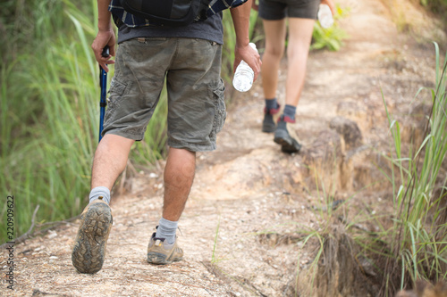 A woman and a man walking a path in a mountain forest. View from the back. Legs in sneakers close-up. Hiking shoes.