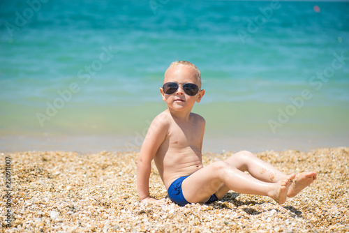  The child sitting on the beach wearing sunglasses