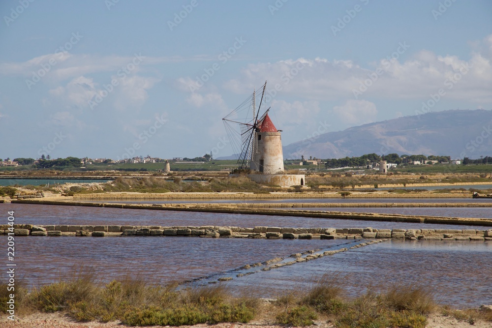 A white lighthouse with a red roof in the middle of the salt marshes of Marsala in Sicily, Italy, on a beautiful sunny day with a blue sky reflecting on the water