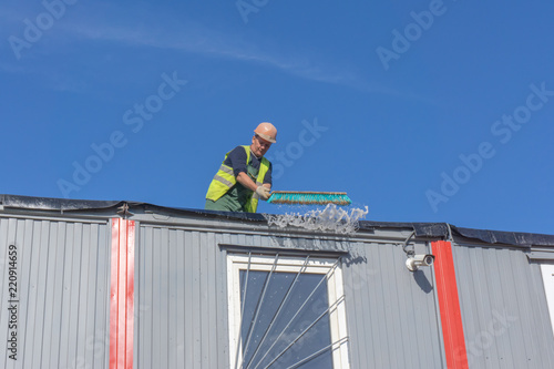 Worker at the construction site cleans the roof of the water with a brush