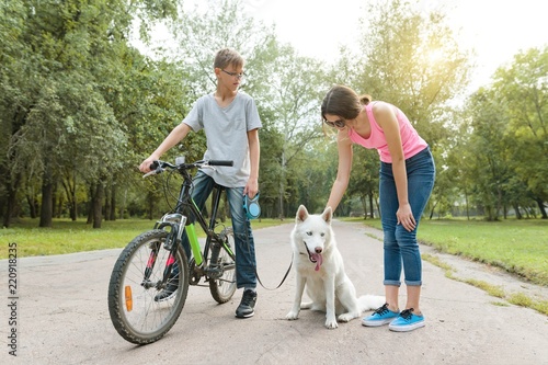 Children teenagers talking, walking the dog in the park on bicycle
