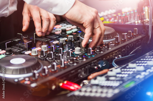 closeup hands of DJ at the control panel wearing in white shirt. disc jockey playing on the professional equipment at night club. concept of clubbing lifestyle