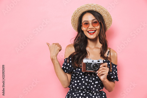 Smiling brunette woman in straw hat and sunglasses pointing away