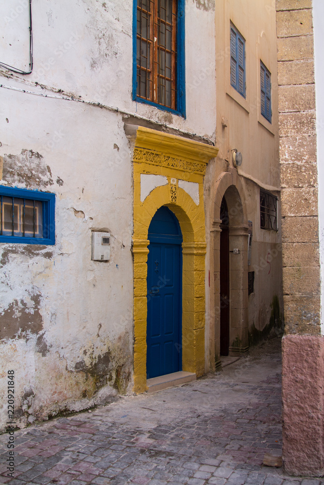 Fototapeta premium An old, covered wooden door against the background of a plastered peeling wall. Moroccan style. Africa, Morocco, Essaouira