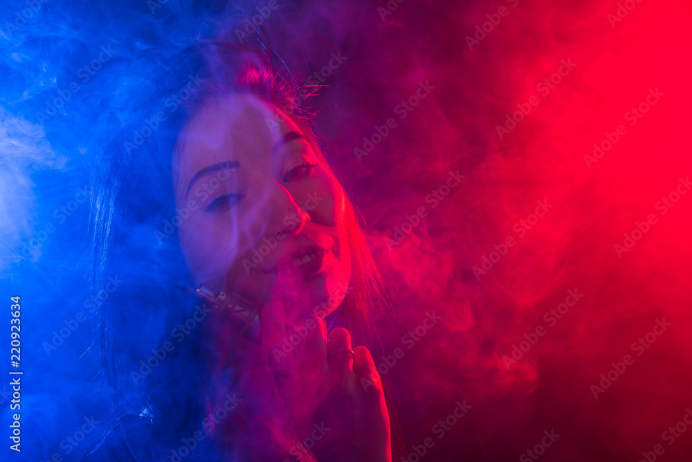 Obraz premium Portrait of asian woman smoking vape or e-cigarette in neon light at dark background.