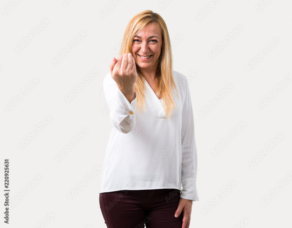 Middle age blonde woman with white shirt presenting and inviting to come with hand. Happy that you came on isolated grey background Middle age blonde woman with white shirt presenting and inviting to come with hand. Happy that you came on isolated grey background