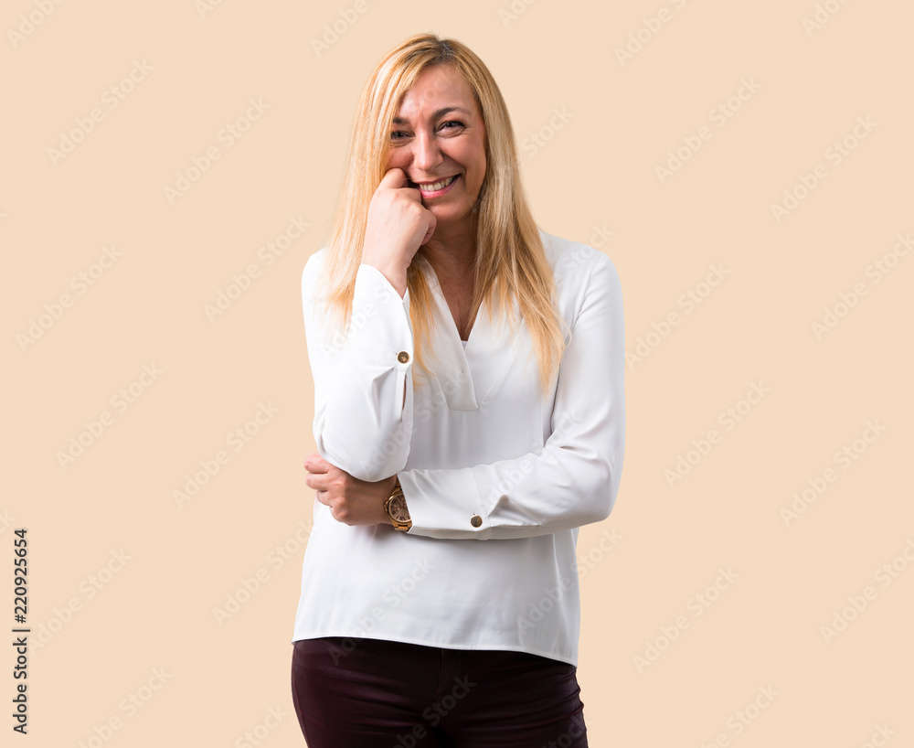 Middle age blonde woman with white shirt smiling with a sweet expression on isolated ocher background Middle age blonde woman with white shirt smiling with a sweet expression on isolated ocher background