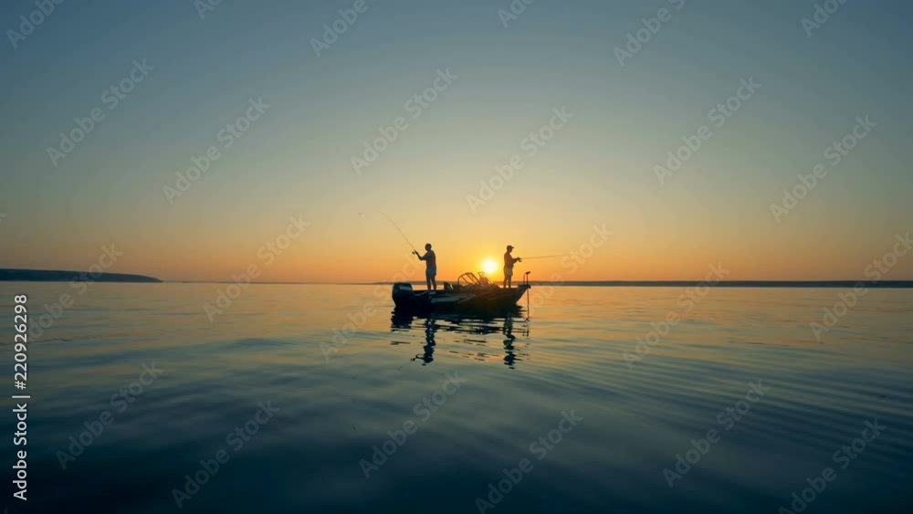 Male silhouettes while fishing from a motorboat during sunrise