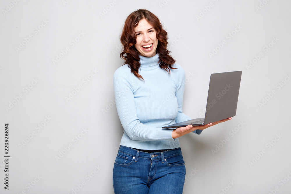 young woman laughing and holding laptop computer against gray background young woman laughing and holding laptop computer against gray background