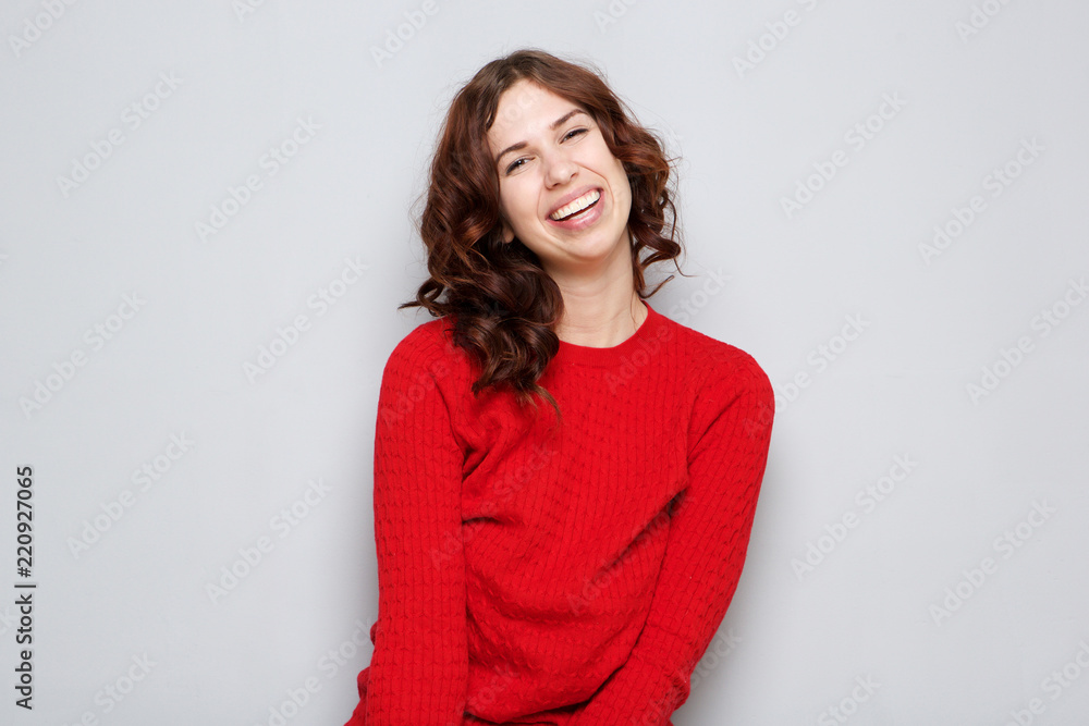Fototapeta premium smiling young woman in red sweater by gray wall