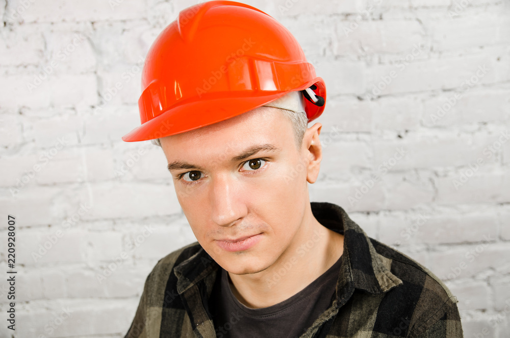 Young worker in a hard hat on a brick wall background Young worker in a hard hat on a brick wall background