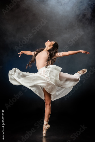 beautiful young ballerina in white skirt dancing on dark background with smoke around © LIGHTFIELD STUDIOS