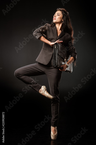 beautiful woman in suit and ballet shoes with suitcase posing on black background