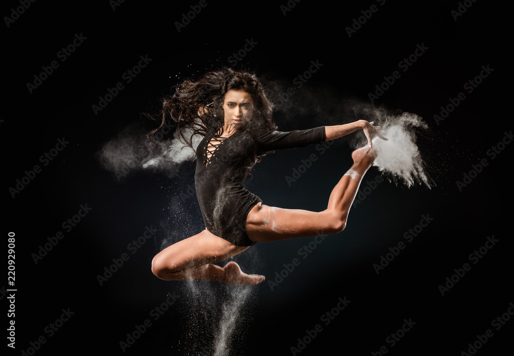 beautiful ballerina in black bodysuit with talc powder jumping on dark background