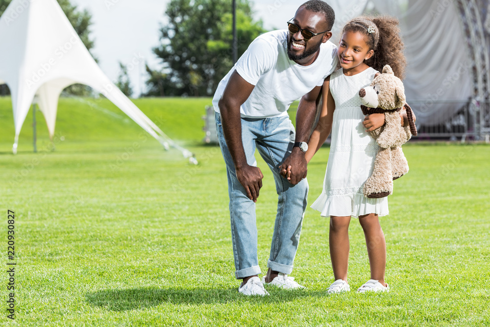 african american father and daughter holding hands in park and looking away african american father and daughter holding hands in park and looking away