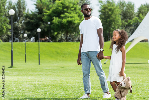 african american father and daughter holding hands and walking in park