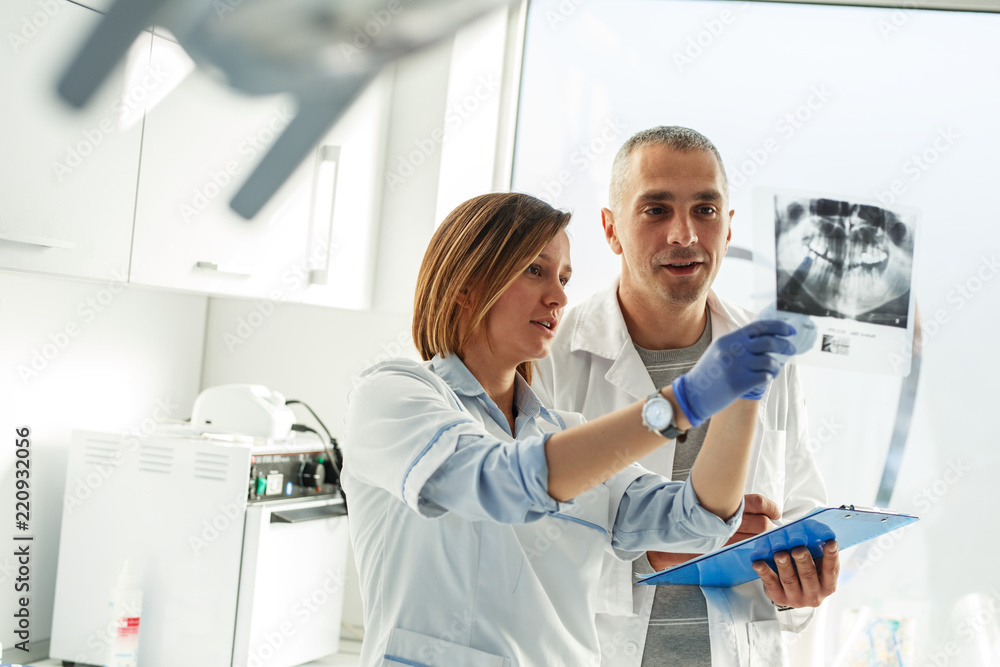 Couple of dentists examining x-ray image of patients teeth. Standing in new bright dentist office. Couple of dentists examining x-ray image of patients teeth. Standing in new bright dentist office.