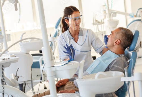 Dentist  in dental office talking with male patient and preparing for treatment.