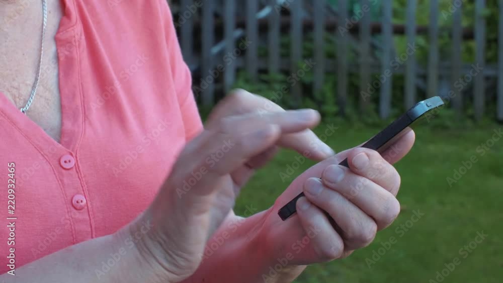 Hands of senior woman touching screen mobile phone in summer garden Hands of senior woman touching screen mobile phone in summer garden