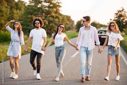 Young happy guys and girls are holding hands and walking on the road on a sunny day