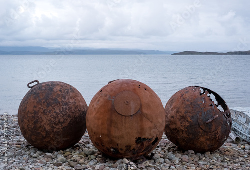 Rusty buoys on the beach at Polbain, north of Ullapool, on the west coast of Scotland. Summer Isles in the background at the point that Loch Broom meets the ocean. photo