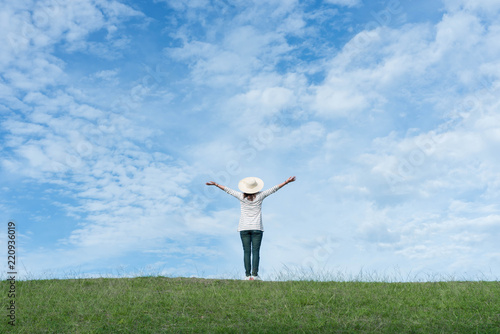 Standing woman raised her hands on the mountain, natural green and beautiful sky.