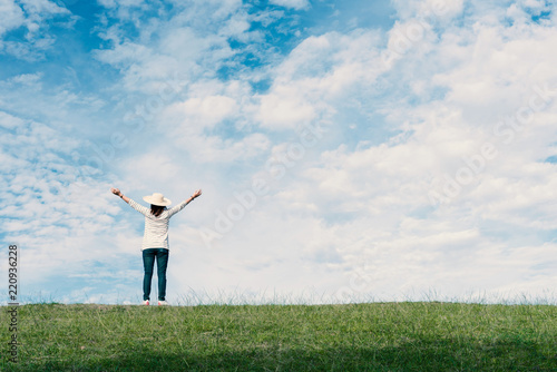 Standing woman raised her hands on the mountain, natural green and beautiful sky.