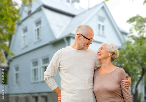 old age, accommodation and real estate concept - happy senior couple hugging over house background