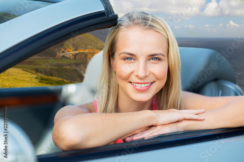 travel, road trip and people concept - happy young woman in convertible car over bixby creek bridge on big sur coast of california background