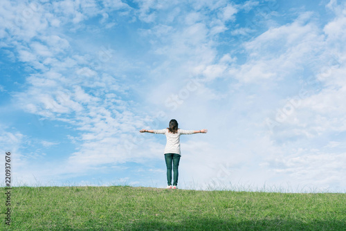 Standing woman raised her hands on the mountain, natural green and beautiful sky.