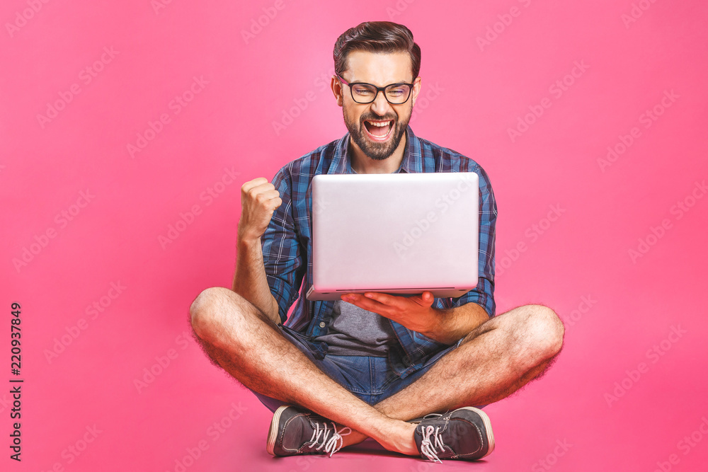 Online working concept. Casual business man relaxed working and browsing internet on laptop computer. Freelance sitting and typing on laptop keyboard at home office. Pink background. - obrazy, fototapety, plakaty 