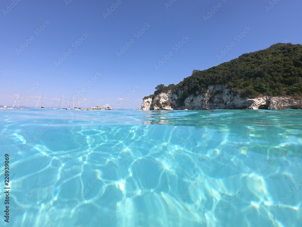 Fototapeta premium Underwater photo of tropical paradise turquoise exotic beach of Voutoumi with sail boats docked in island of Antipaxos, Ionian, Greece