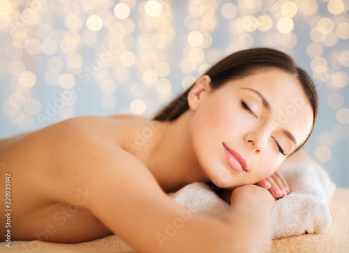 wellness and beauty concept - close up of beautiful woman at spa over holidays lights background