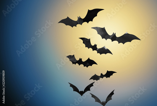 halloween and scary concept - black bats flying in moonlight over night sky background