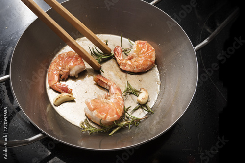 fresh king prawns roasted with rosemary and garlic in an iron pan on a black stove with copy space