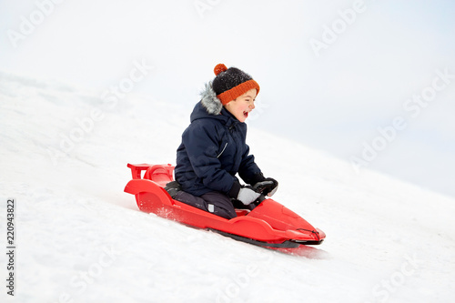 Obraz na plátně childhood, sledging and season concept - happy little boy sliding on sled down s