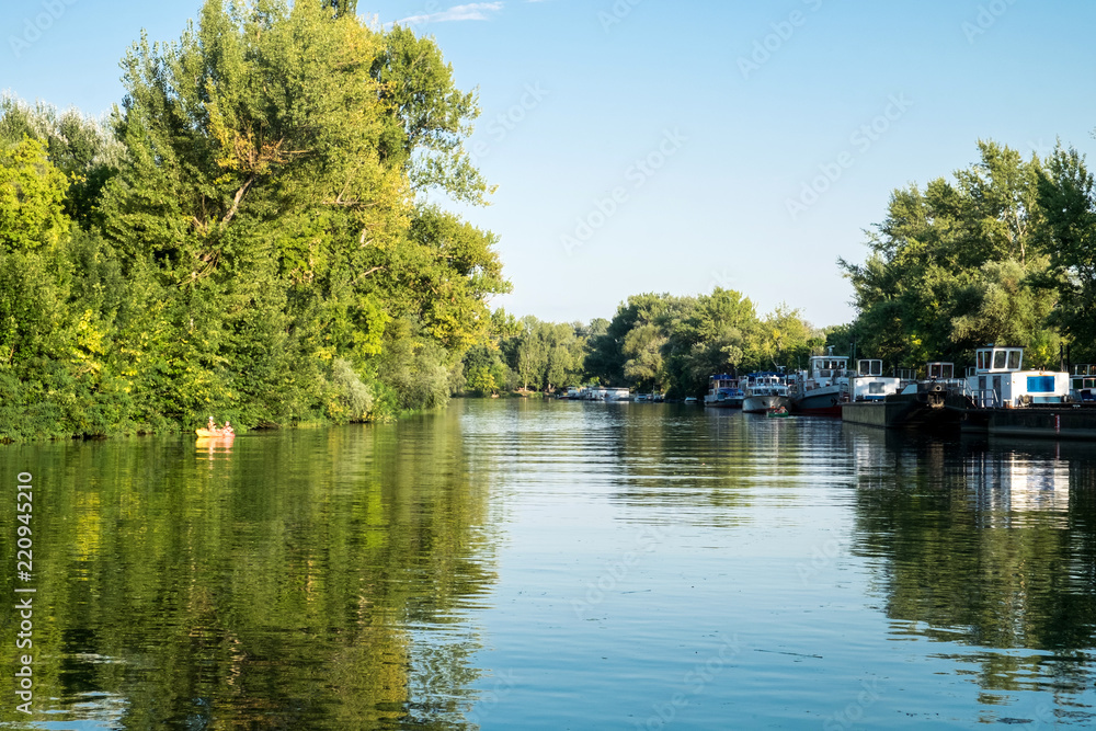 The sunny summer day on the picturesque banks of the Tisza river in Tokaj, Hungary - a beautiful countryside landscape with reed, boat and reflection on water mirror The sunny summer day on the picturesque banks of the Tisza river in Tokaj, Hungary - a beautiful countryside landscape with reed, boat and reflection on water mirror