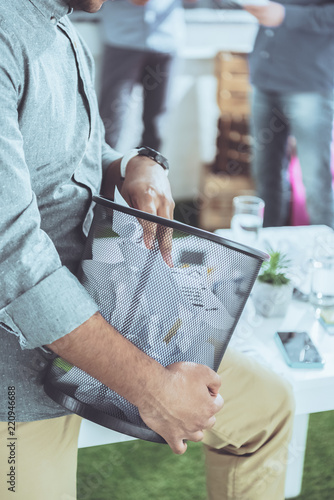 partial view of businessman holding trash bucket with papers, business teamwork