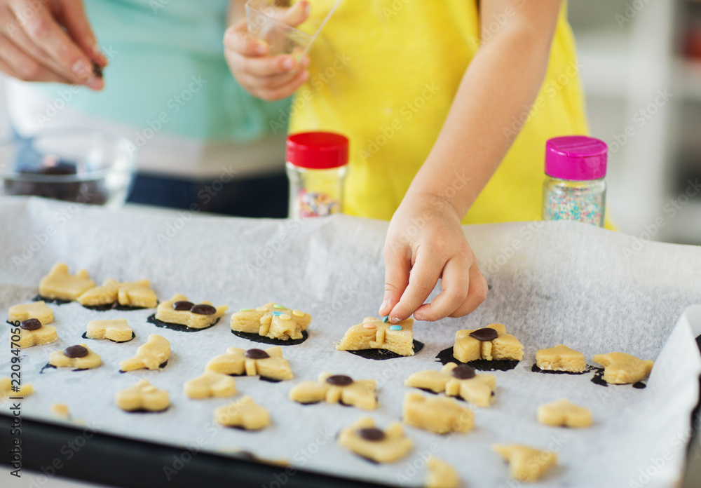 family, cooking and baking concept - mother and little daughter with sprinkles decorating cookies on tray at home kitchen family, cooking and baking concept - mother and little daughter with sprinkles decorating cookies on tray at home kitchen