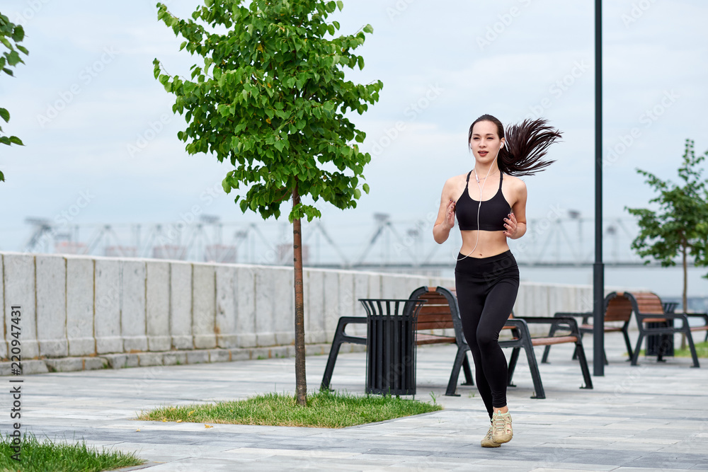 Running asian woman on the waterfront. Morning jogging. The athlete trains