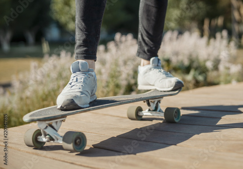 Close up of young man in sneakers riding longboard or skateboard in the park.