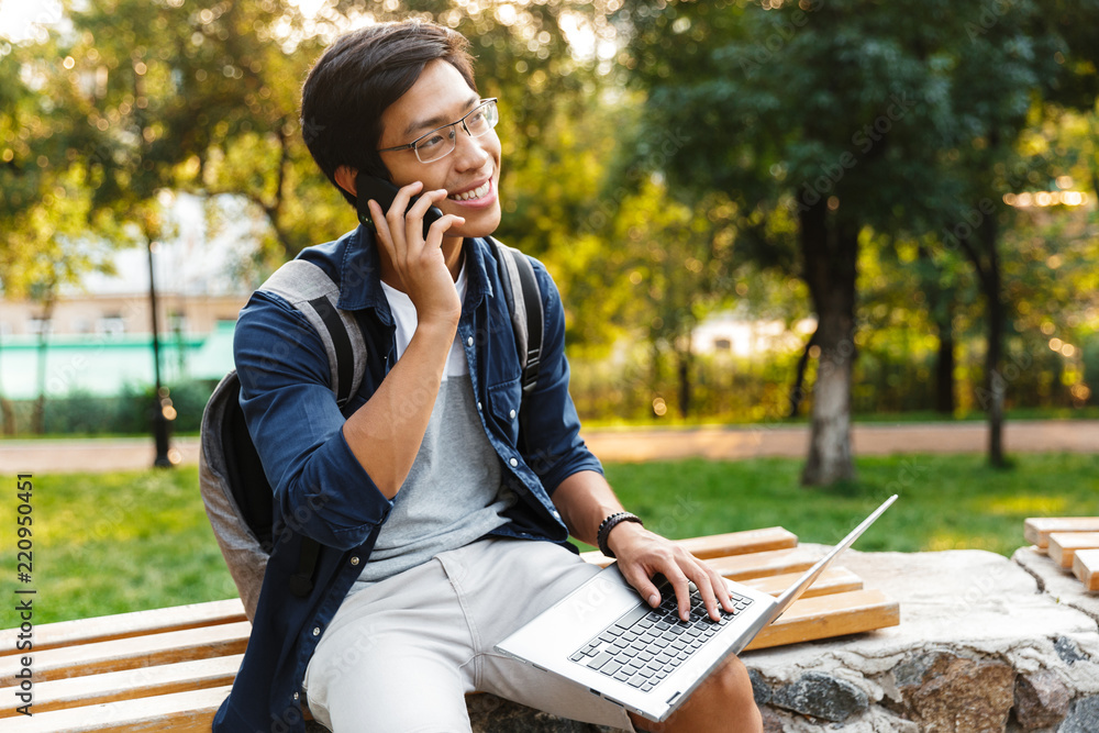 Happy asian male student in eyeglasses talking by smartphone Happy asian male student in eyeglasses talking by smartphone