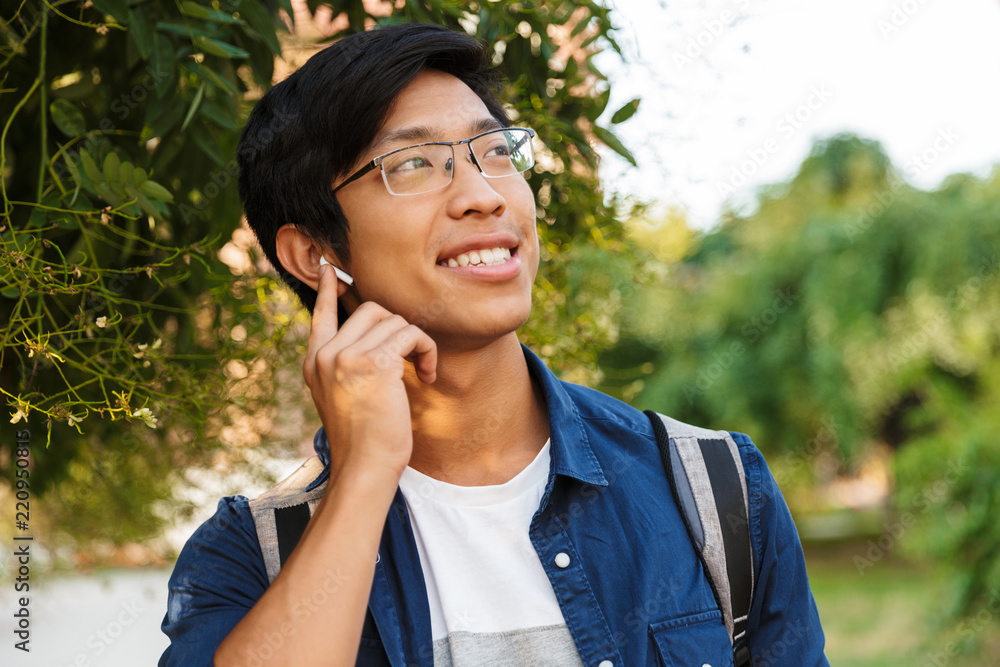 Image of Smiling asian male student in eyeglasses listening music Image of Smiling asian male student in eyeglasses listening music