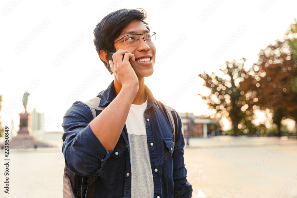 Joyful asian male student in eyeglasses talking by smartphone Joyful asian male student in eyeglasses talking by smartphone