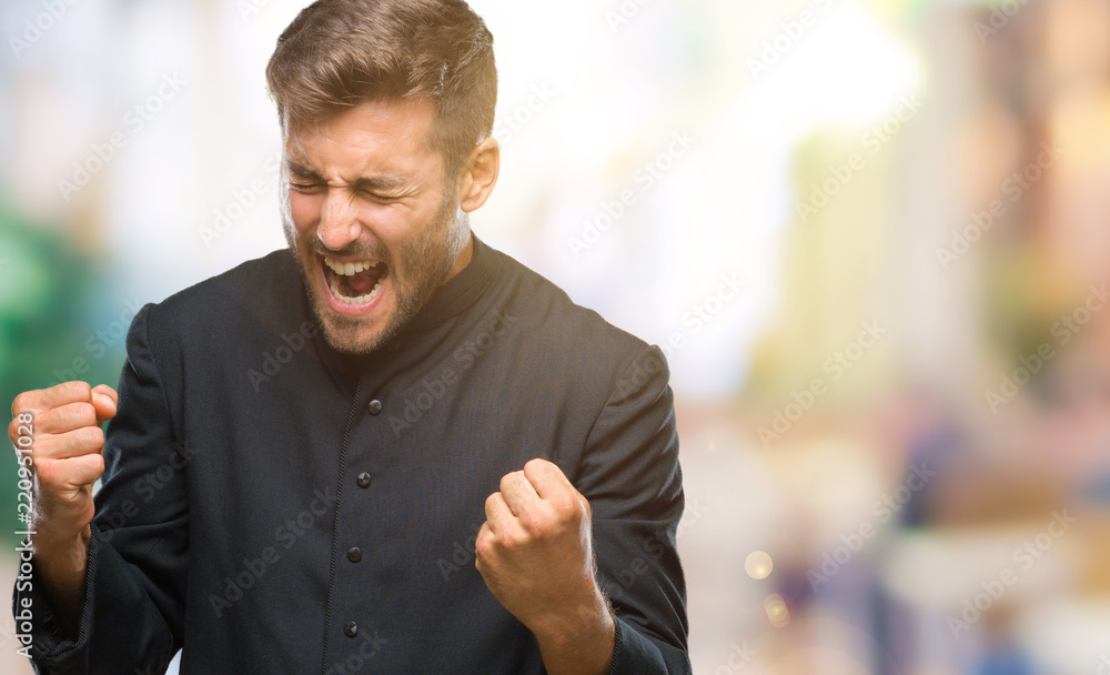 Naklejka premium Young catholic christian priest man over isolated background very happy and excited doing winner gesture with arms raised, smiling and screaming for success. Celebration concept.
