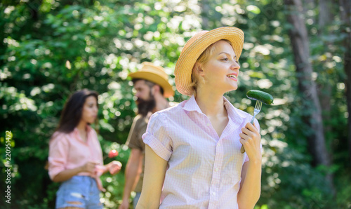 Friends eating food picnic. Nature conditions cause great appetite. Lady vegetarian in straw hat eats green organic cucumber. Vegetable organic nutrition for vegetarian. Girl holds fork with cucumber