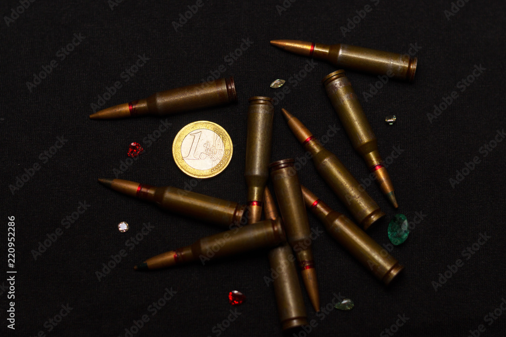 Rifle ammo around one euro coin wigh gemstones on black background. Symbolizes the war for money and one of the world's problems. Rifle ammo around one euro coin wigh gemstones on black background. Symbolizes the war for money and one of the world's problems.