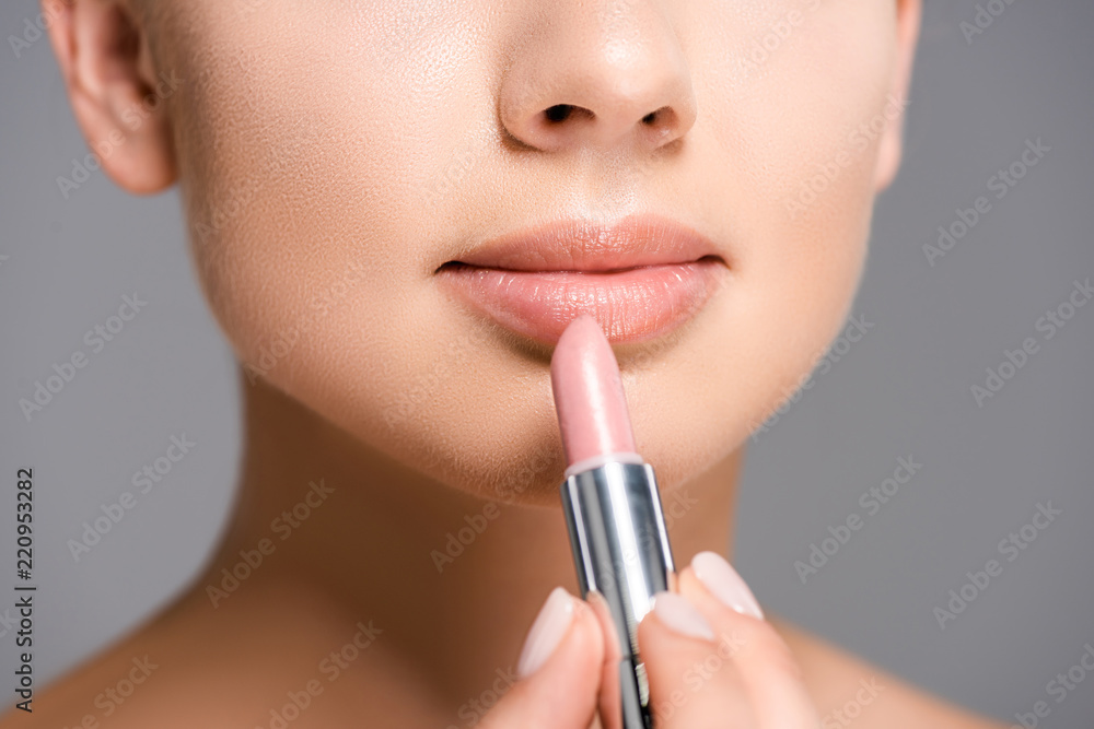 partial view of woman applying nude lipstick isolated on grey